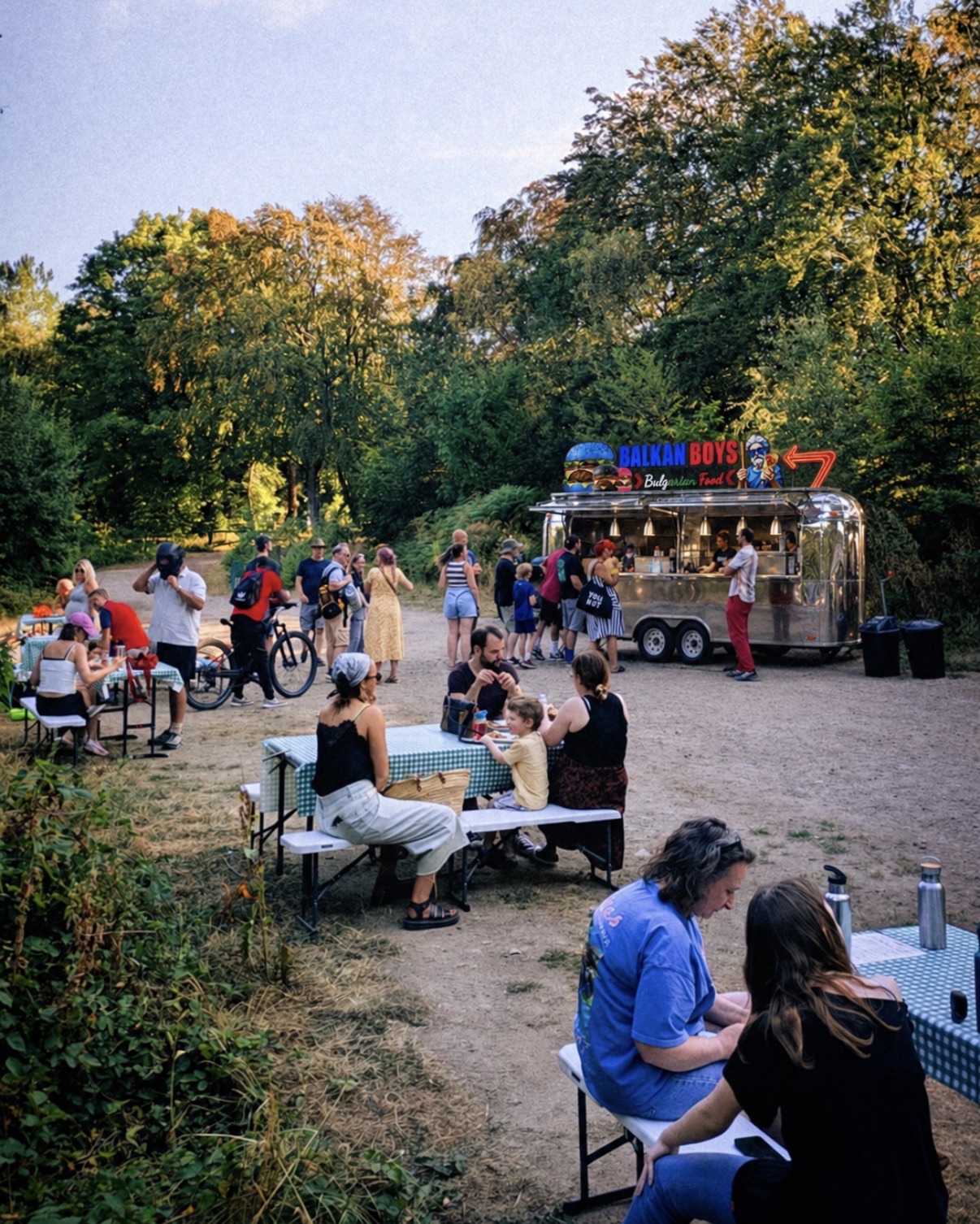The ballkanboyz silver trailer surrounded by festivalgoers and picnic tables beneath the trees